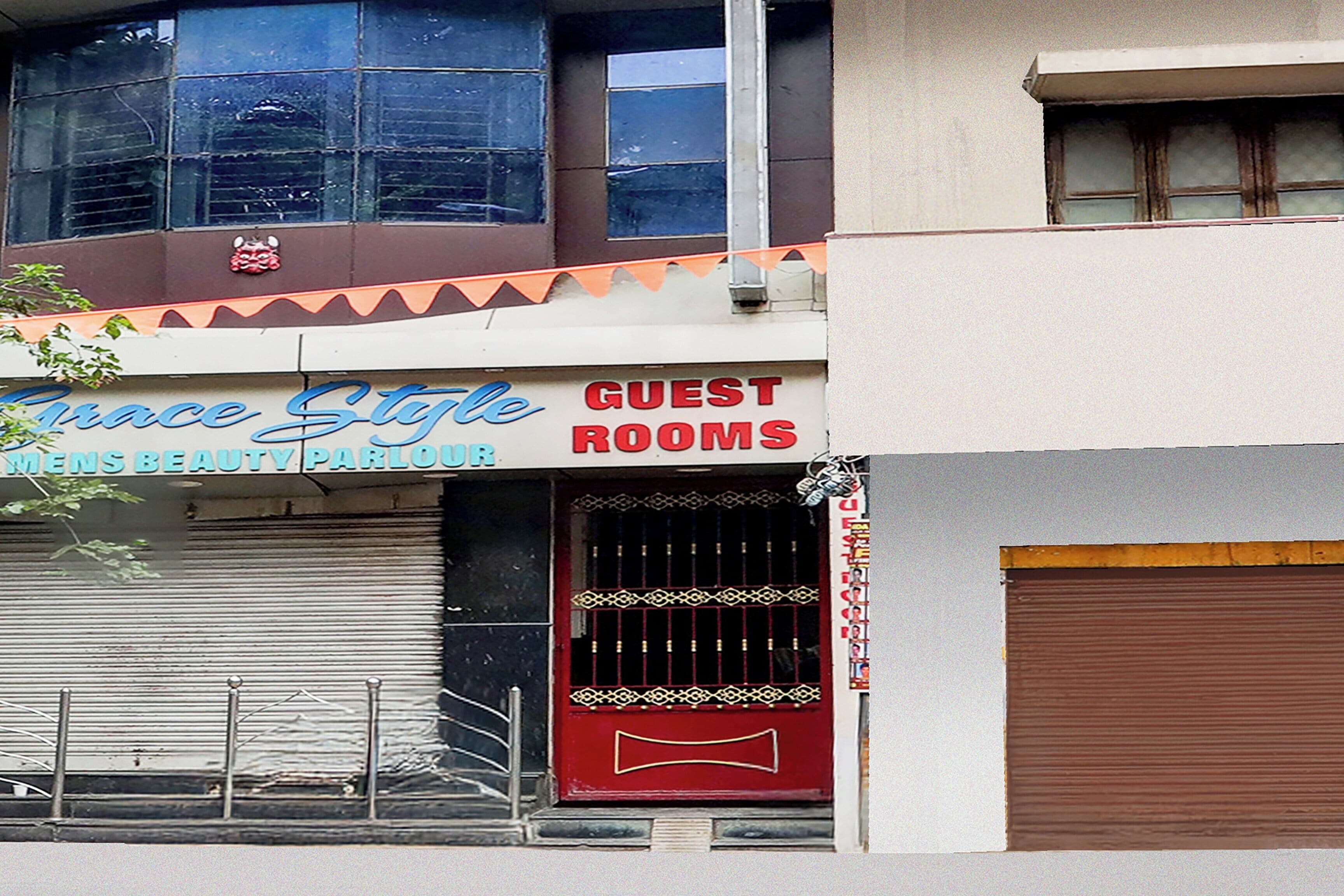 Um edifício com uma placa indicando 'Grace Stile Mens Beauty Parlour' e 'Guest Rooms' acima de uma porta com persiana fechada.