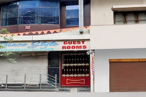 Un edificio con un letrero que indica 'Grace Stile Mens Beauty Parlour' y 'Habitaciones para Huéspedes' sobre una puerta con una persiana cerrada.