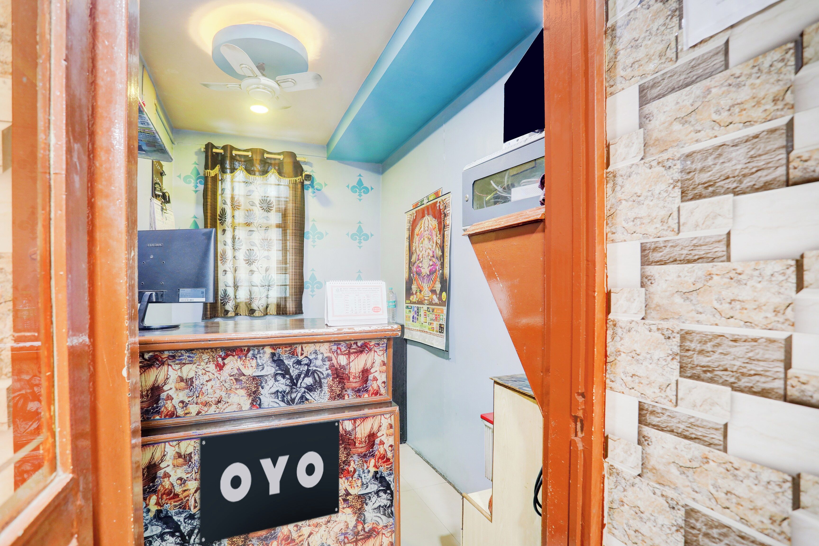 Un área de recepción con un cartel que dice 'OYO', un ventilador de techo, una cortina decorativa y una pared con un diseño estampado.