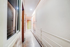 A corridor with a tiled floor, a wooden door, and a white railing.