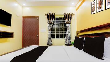 Quarto de hotel com cama, televisão presa na parede, janela com cortinas e porta.