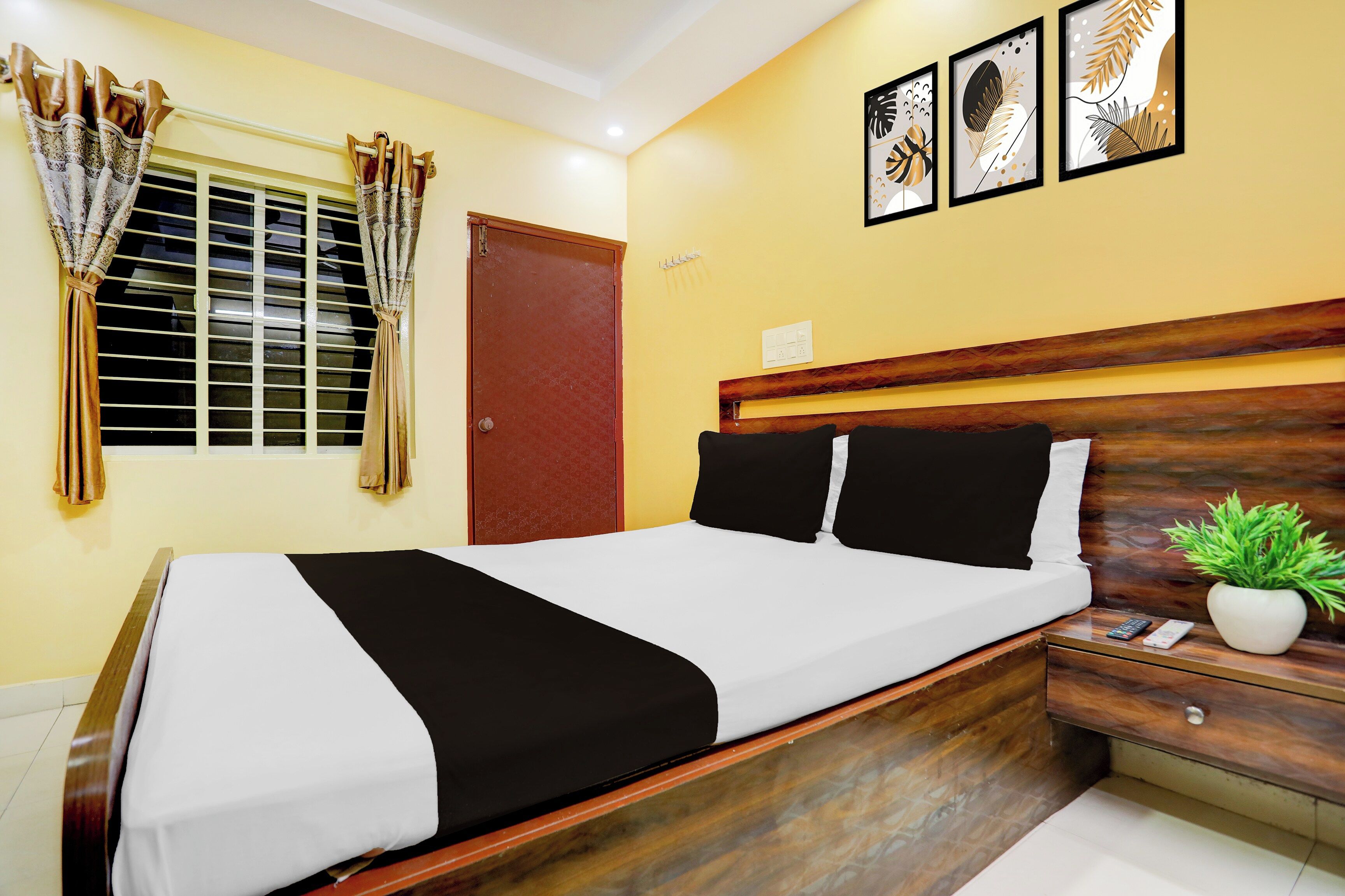 Una habitación de hotel con una cama, una mesita de noche, una planta en maceta y una ventana con cortinas.