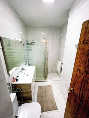 A modern bathroom with a glass shower enclosure, a wooden vanity, and a white toilet. - Charming Tangier Apartment Central, Iconic, and Comfortable (Tangier)