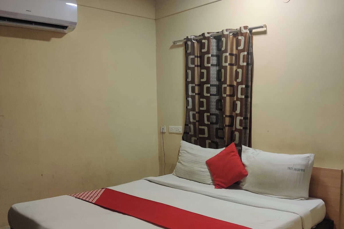 A single bed with a red bedspread, white pillows, and a patterned curtain.