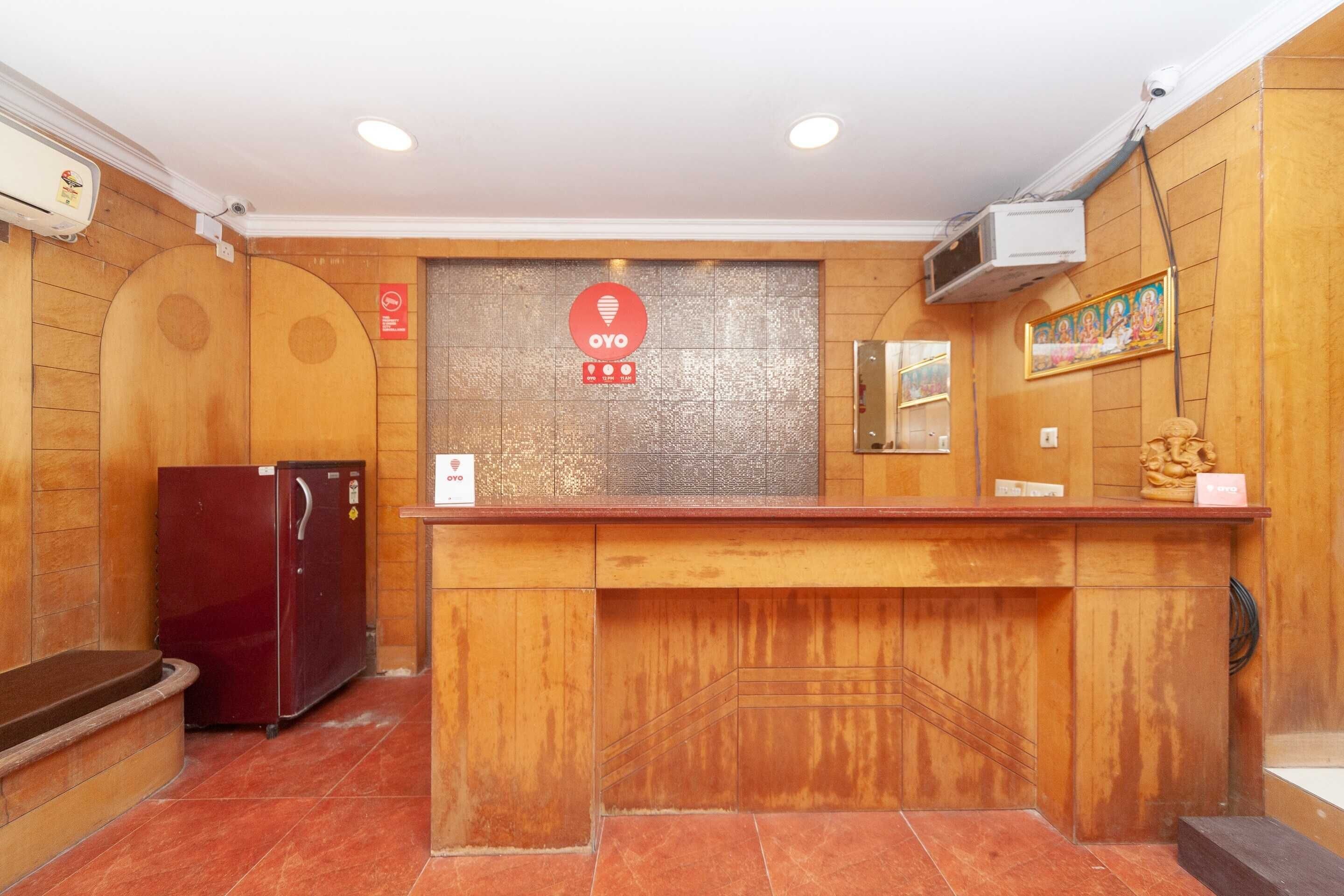 A reception desk with a wooden counter, a refrigerator, and a wall-mounted security camera.