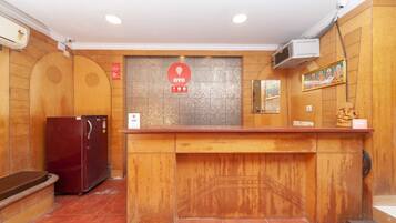 A reception desk with a wooden counter, a refrigerator, and a wall-mounted security camera.