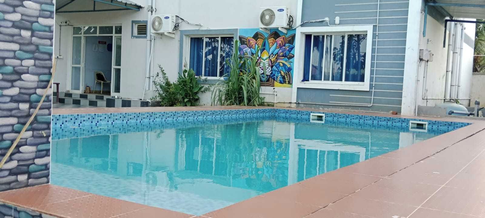 A swimming pool with a tiled edge, a mural on the adjacent wall, and a covered area with a chair.