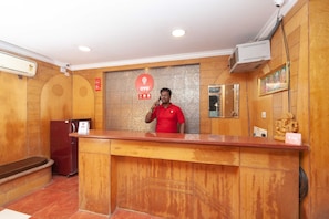 A reception desk with a wooden finish, a security camera above, and a sign with the OYO logo. - Hotel O CANARIES RETIREES RESIDENCY (Vanur)