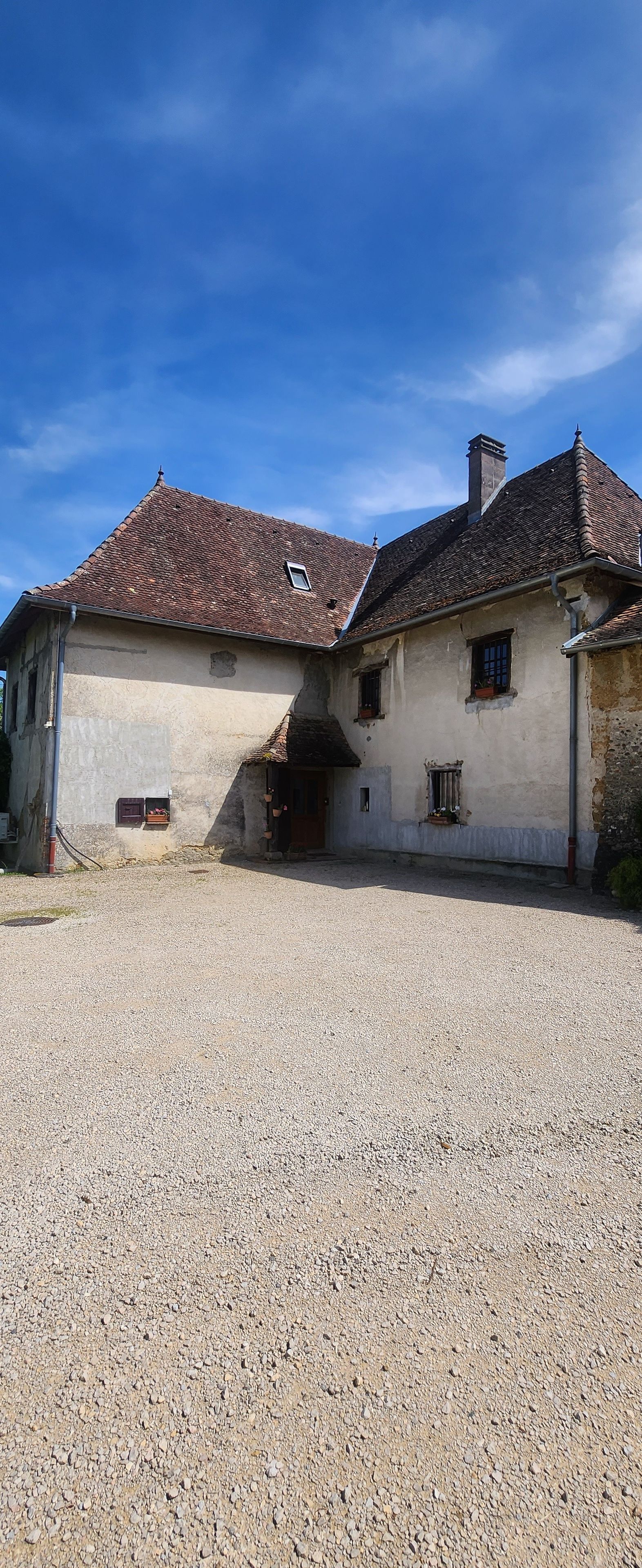 Un bâtiment avec un toit recouvert de tuiles, une allée en gravier et une petite fenêtre.