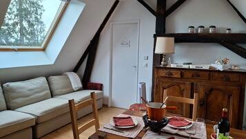 A cozy loft bedroom with a sloped ceiling, a skylight, a wooden dining table set for two, a sofa, and a cabinet with kitchenware.