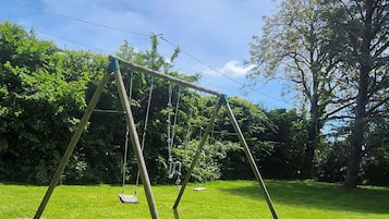 A swing set in a grassy park area with trees in the background.