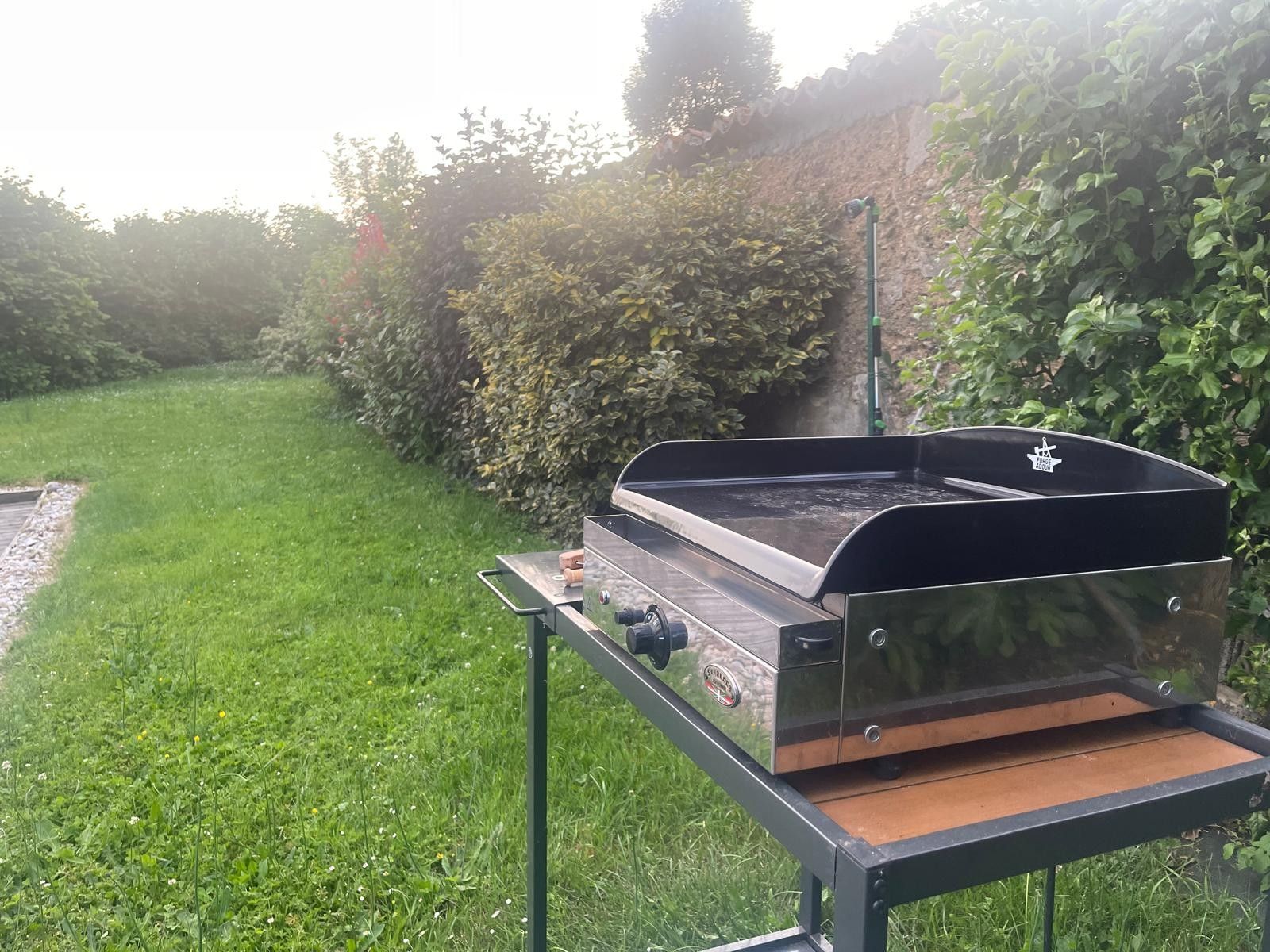 Un barbecue portable, posé sur un support métallique, dans un espace extérieur recouvert d’herbe.