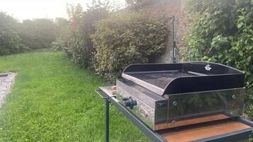Un barbecue portable, posé sur un support métallique, dans un espace extérieur recouvert d’herbe.