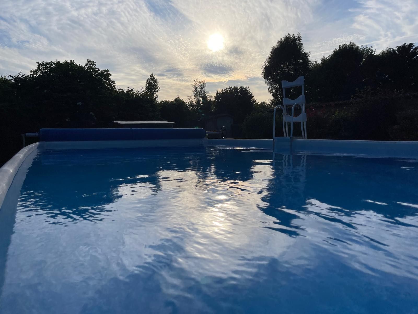 A swimming pool with clear water, surrounded by trees and a cloudy sky.