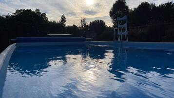 A swimming pool with clear water, surrounded by trees and a cloudy sky.