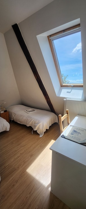 Una habitación con techo inclinado, cama, escritorio y ventana con vista al cielo.