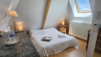 A bedroom with a skylight, a bed with white bedding, a nightstand with a lamp, a wooden dresser, and a water dispenser on the counter.