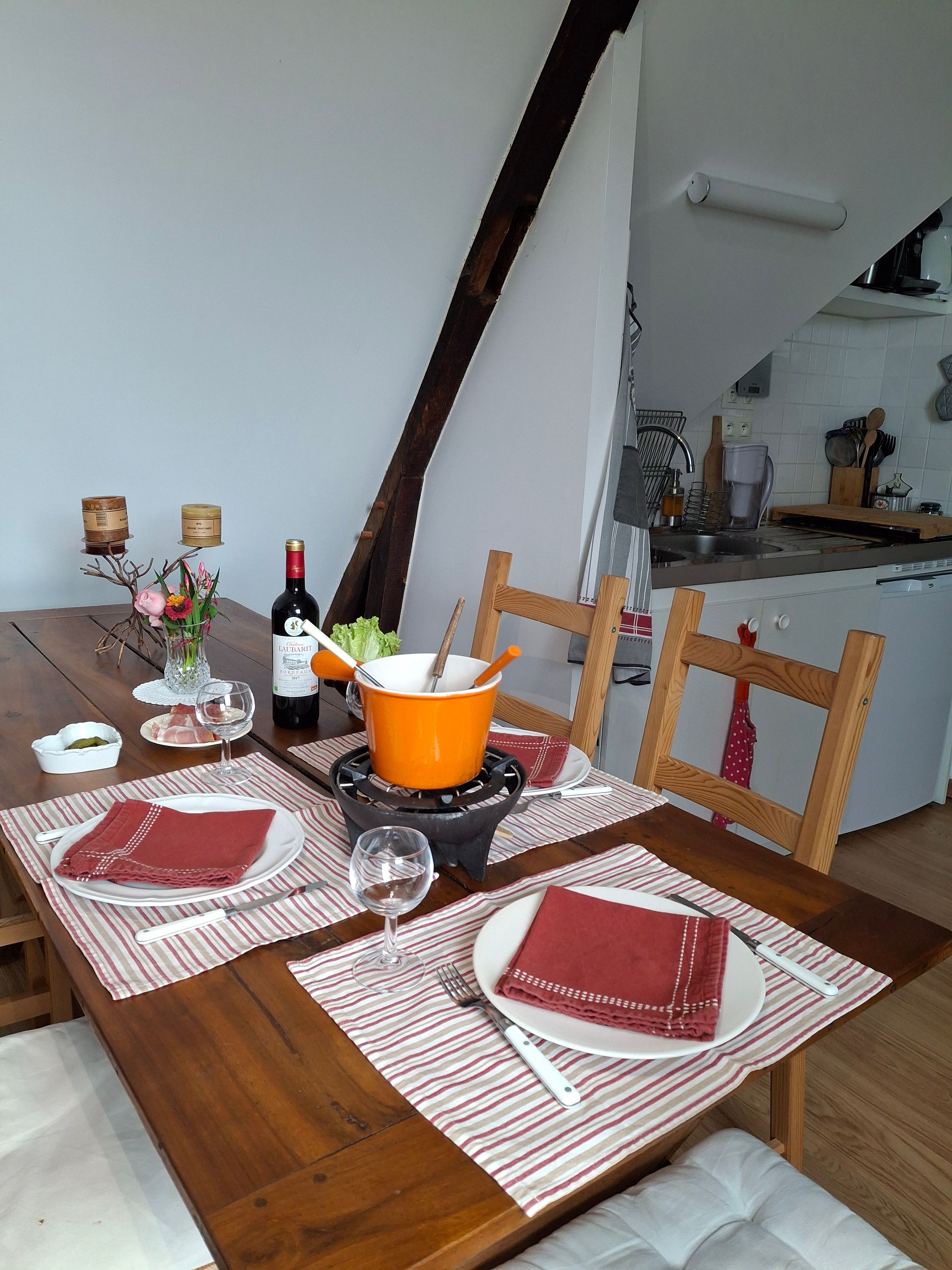 A dining table set with a red and white striped placemat, a white plate, a red napkin, a wine glass, and a bottle of wine.