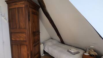A bedroom with a wooden wardrobe, a single bed, a bedside table with a lamp, and a window.