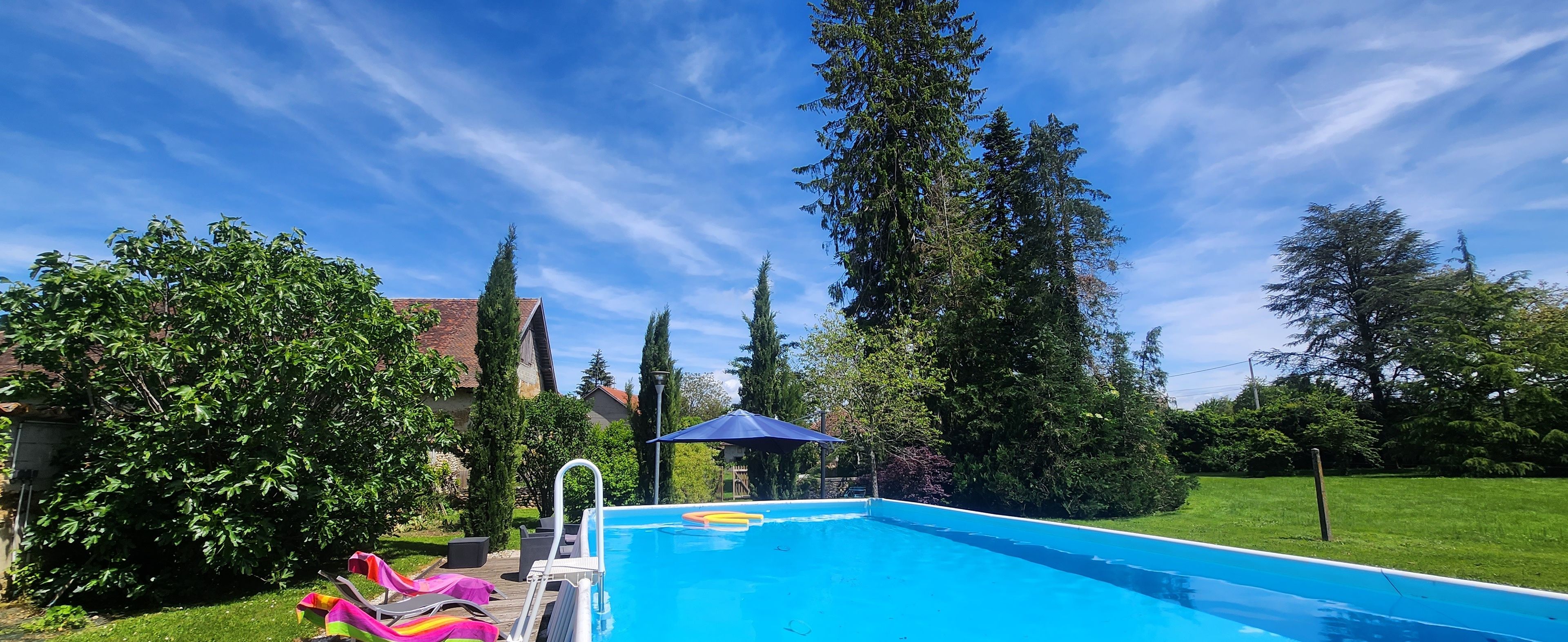 Una piscina con terraza de madera, sillas de descanso y zona cubierta.