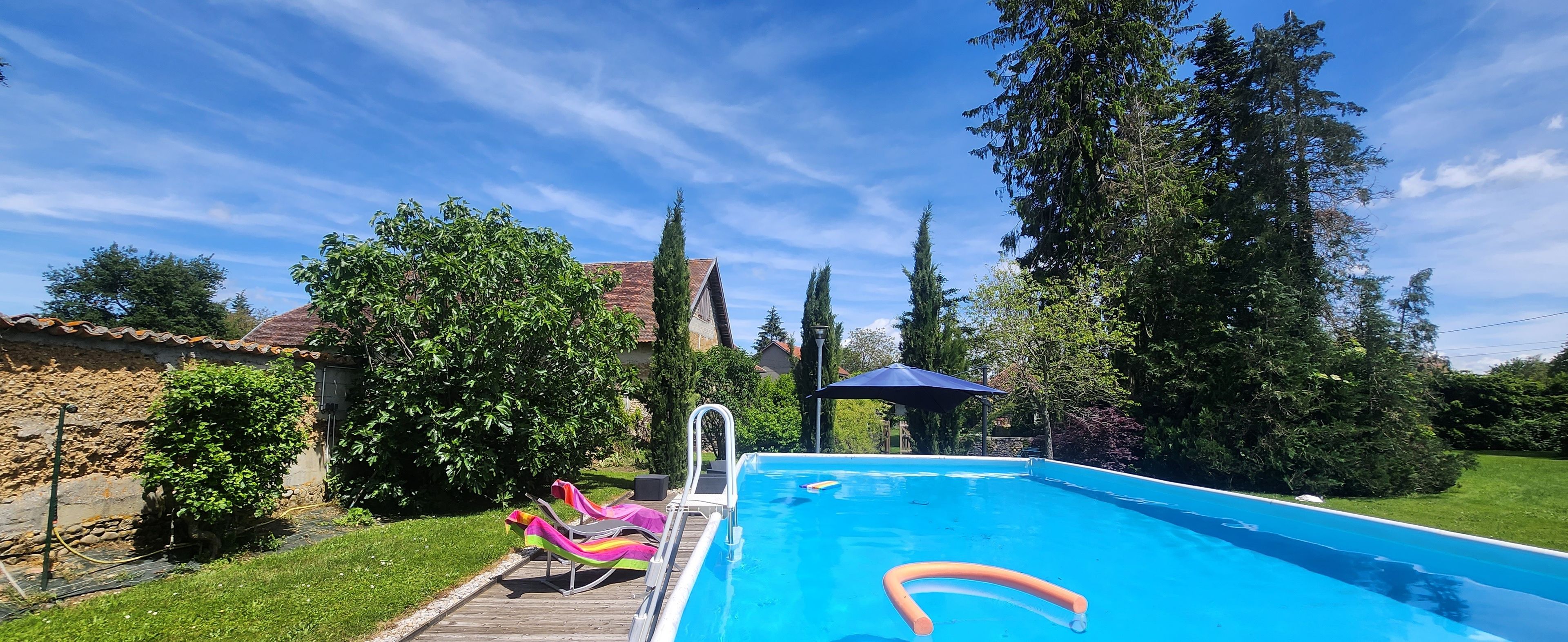 A swimming pool with a wooden deck, lounge chairs, and a sun umbrella.