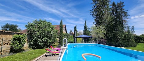 A swimming pool with a wooden deck, lounge chairs, and a sun umbrella.