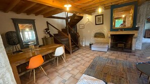 Un interior rústico con una escalera de madera, una chimenea y un comedor con mesa y sillas.