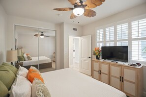 Ein Hotelzimmer mit Bett, Fernseher, Holzschrank, Deckenventilator und großem Fenster.