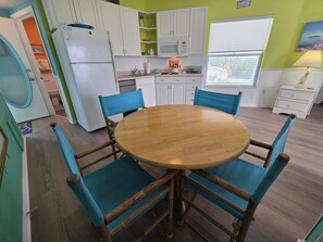 A kitchen with white cabinets, a round wooden table, and blue chairs. - Siesta Sunset Royale #6 1 Bedroom Apts (Siesta Key)