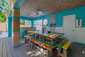 Eine Terrasse im Freien mit einem Holztisch und Bänken, einem Deckenventilator und einer Tür mit Fenster.