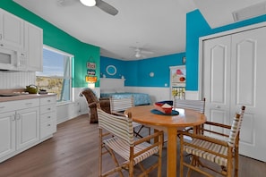 A kitchen with white cabinets, a dining table with chairs, and a blue accent wall. - Siesta Sunset Royale #3 1 Bedroom Apts (Siesta Key)