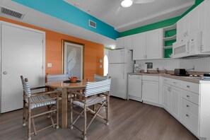 A kitchen with white cabinets, a dining table with striped chairs, and a painting on the wall. - Siesta Sunset Royale #3 1 Bedroom Apts (Siesta Key)