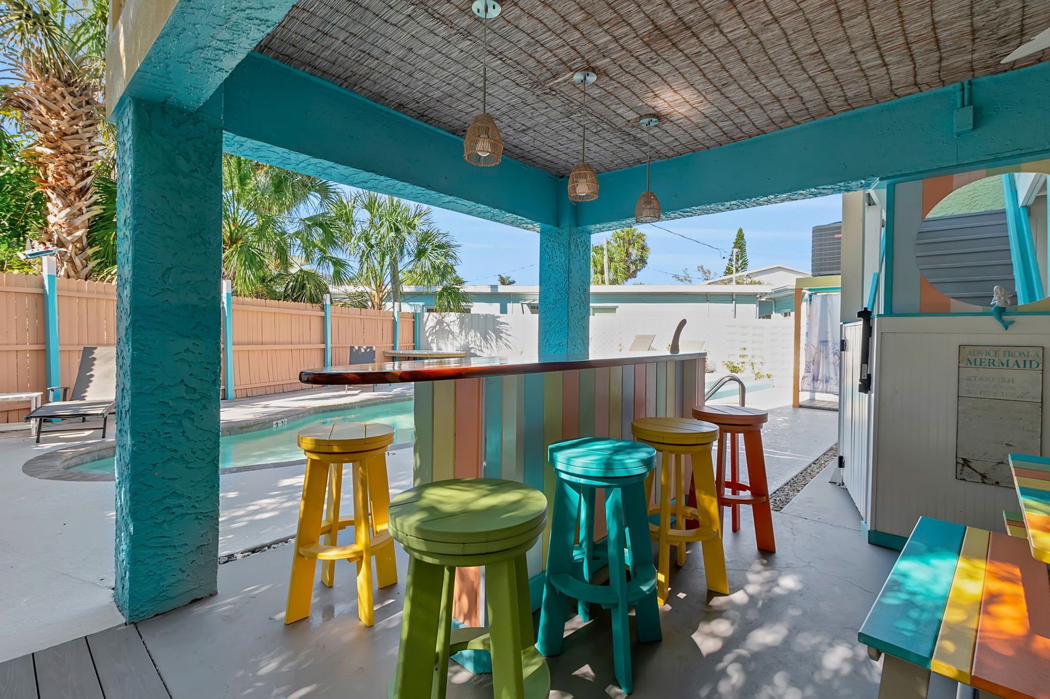 A covered outdoor area with a pool, colorful stools, and a table.