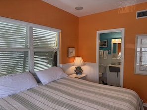 A bedroom with a bed, a nightstand, a lamp, and a bathroom visible through an open door. - Siesta Sunset Royale #2 2 Bedroom Apts (Siesta Key)
