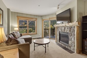 A living room with a fireplace, a sofa, a coffee table, and a large window with a view of a mountain landscape. - Cs322 Copper Springs 2 Bedroom Condo (Copper Mountain)
