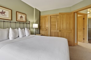 A bedroom with a large bed, a nightstand, a lamp, and two wooden doors. - Cs322 Copper Springs 2 Bedroom Condo (Copper Mountain)