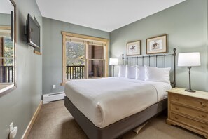 Une chambre à coucher avec un grand lit, une table de chevet avec des lampes, une commode et une fenêtre donnant sur des arbres.