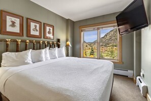 A hotel room with a large bed, a flat-screen TV mounted on the wall, and a window offering a view of a mountainous landscape. - Cs322 Copper Springs 2 Bedroom Condo (Copper Mountain)