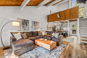 Ein modernes Wohnzimmer mit einem Ecksofa, einem Holztisch und abstrakter Wandkunst.