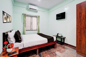 Habitación de hotel con cama, una mesita de noche, televisor montado en la pared, equipo de aire acondicionado y ventana con cortinas.