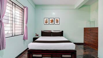 A bedroom with a bed, a nightstand, a dresser, and a window with curtains. There are three framed pictures on the wall.