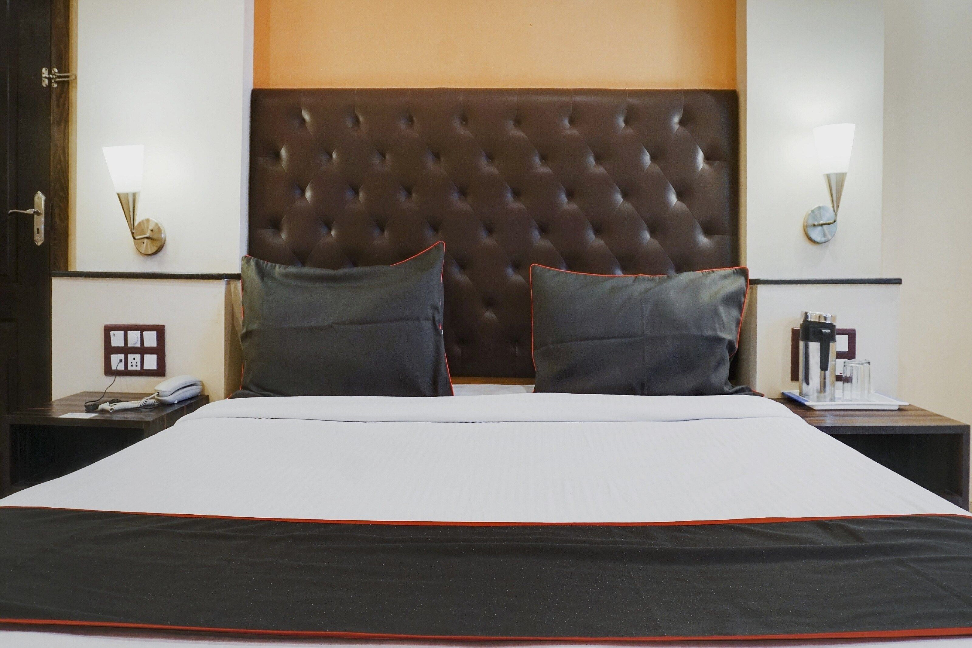 Habitación de hotel con una cama grande, dos mesitas de noche, un reloj de pared y un enchufe.