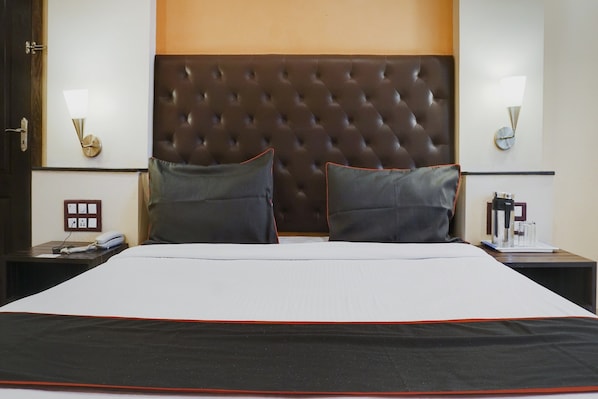 Habitación de hotel con una cama grande, dos mesitas de noche, un reloj de pared y un enchufe.