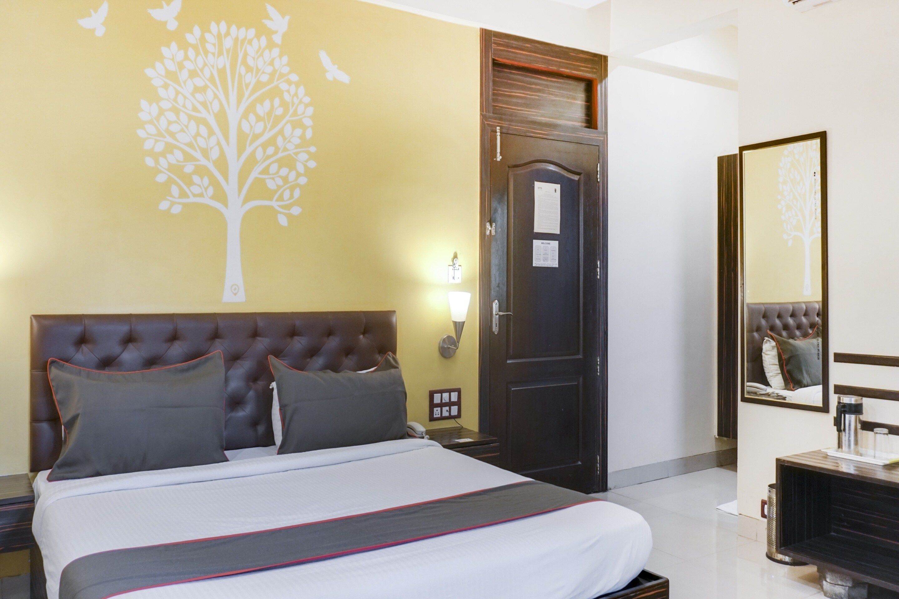 A hotel room with a bed, a wall-mounted light, a door, and a mirror.