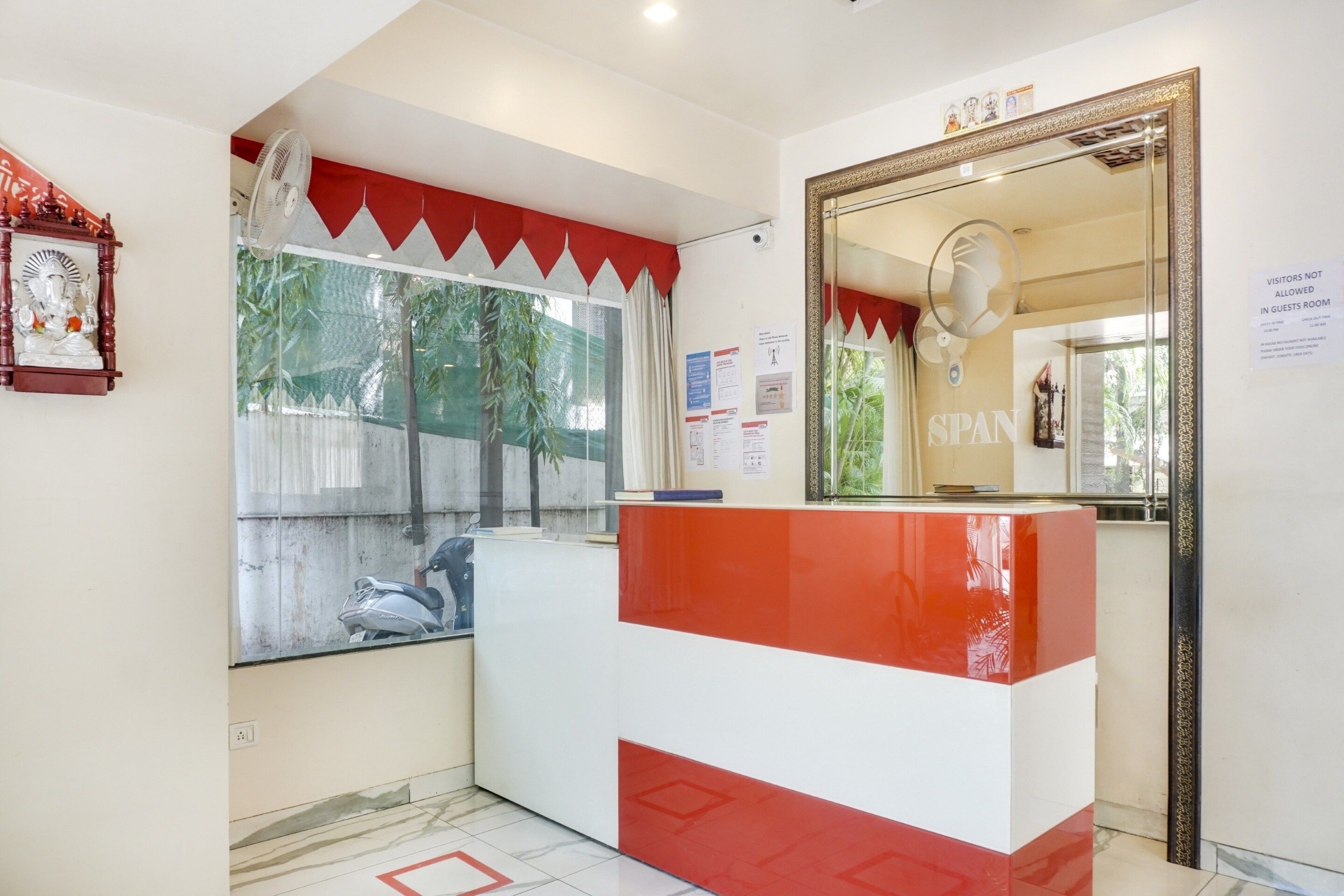 A reception area with a red and white counter, a large mirror, and a statue on the wall.