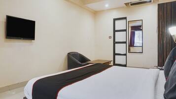 Habitación de hotel con cama, escritorio, silla, televisor de pantalla plana, espejo y ventana con cortinas.
