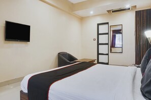 Une chambre d’hôtel comprenant un lit, un bureau, une chaise, un téléviseur à écran plat, un miroir et une fenêtre avec des rideaux.