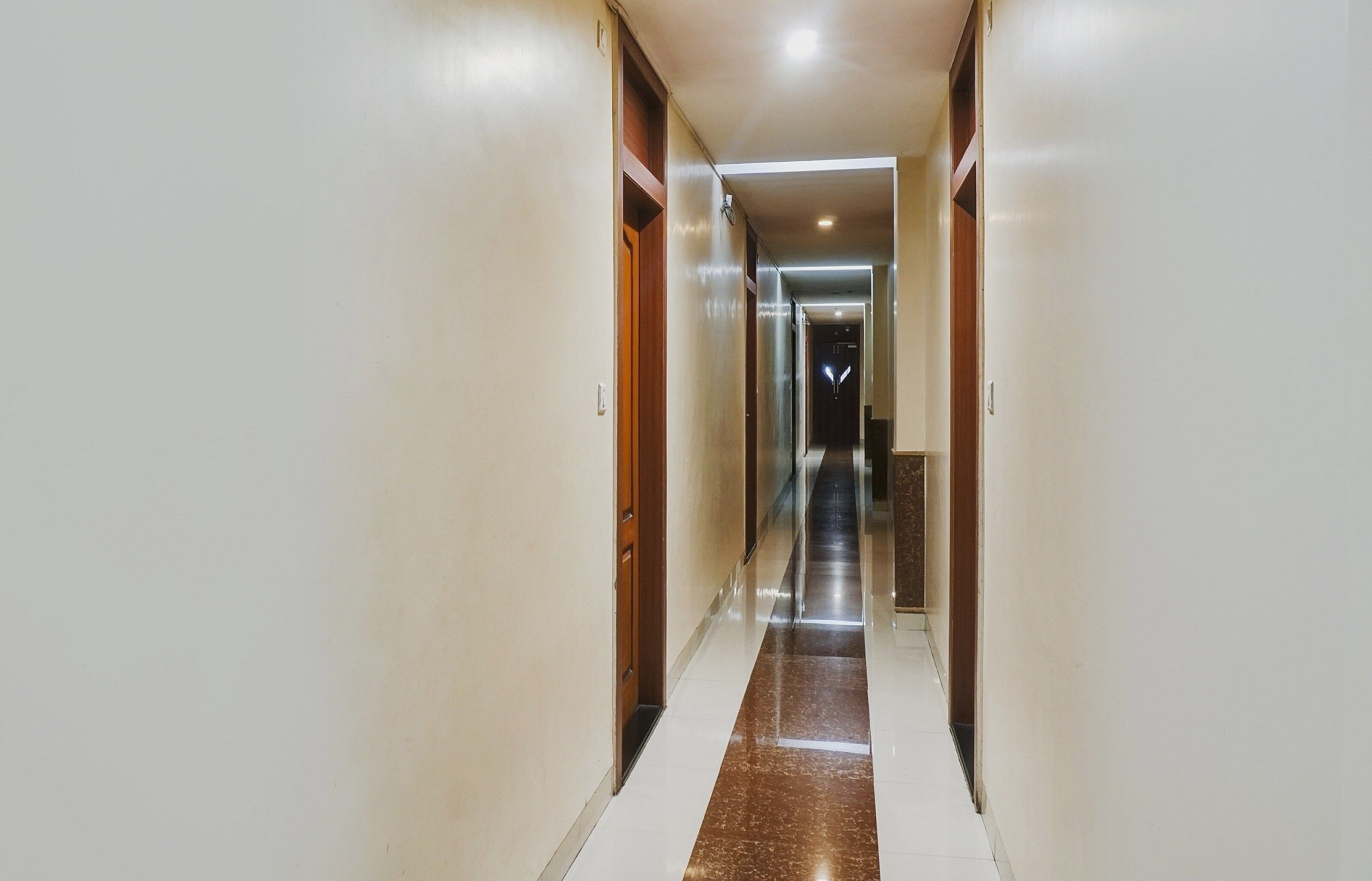 Un pasillo de hotel con puertas a ambos lados, suelo de baldosas y un accesorio de iluminación al final.