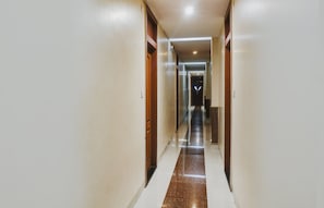 Un pasillo de hotel con puertas a ambos lados, suelo de baldosas y un accesorio de iluminación al final.
