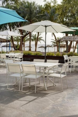 Un espacio patio al aire libre con mesas y sillas blancas, sombrillas y vistas al mar.